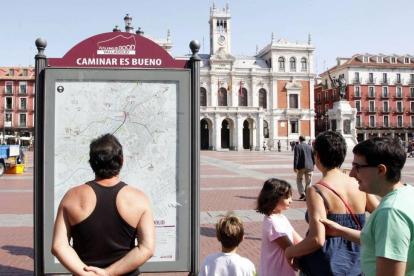 Una familia de turistas observa el panel informativo de las rutas 'Caminar es bueno' en la Plaza Mayor de Valladolid-Ical