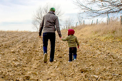 Un padre pasea con su hijo de la mano en un campo de cultivo.