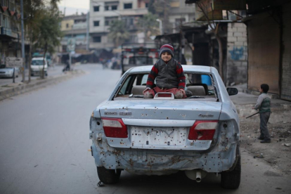 Un niño sirio sentado sobre un coche dañado por las explosiones del este de Ghouta.-AMER ALMOHIBANY