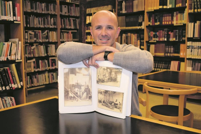 Enrique Bravo con un libro de fotografías antiguas que muestran el interior del obrador de Fontaneda en una de las salas de la biblioteca de Aguilar de Campoo.-E.M.