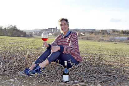 La enóloga María Pinacho se sienta sobre sarmientos mientras sujeta una copa de su vino en el paraje de los mimbreros, con el municipio de Mucientes al fondo.-ARGICOMUNICACIÓN