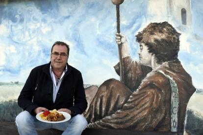 César Acero, con un plato del menú, junto al mural de temática jacobea de su complejo hostelero-ARGICOMUNICACIÓN