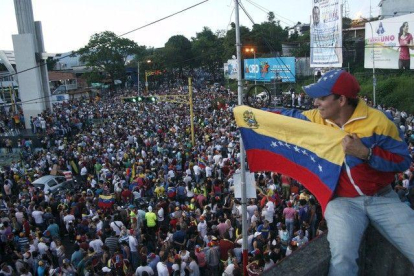 Un simpatizante de la oposición ondea una bandera venezolana ante cientos de personas congregadas para celebrar los resultados electorales en Venezuela.-REUTERS