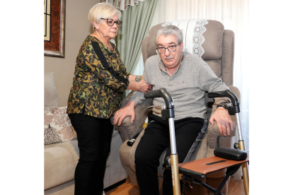 Ludi ayuda a su marido Miguel Ángel a sentarse en el sillón, en su casa en Valladolid. J.M. LOSTAU
