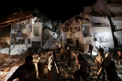 Civiles y miembros de la defensa civil buscan supervivientes en un edificio destrozado por los bombardeos aéreos, este lunes por la noche, en Idleb.-REUTERS / KHALIL ASHAWI