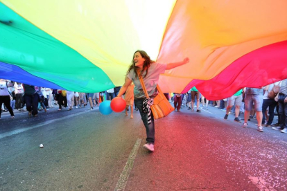Una joven corre por debajo de la bandera arcoíris en una manifestación LGTBI.-EL MUNDO