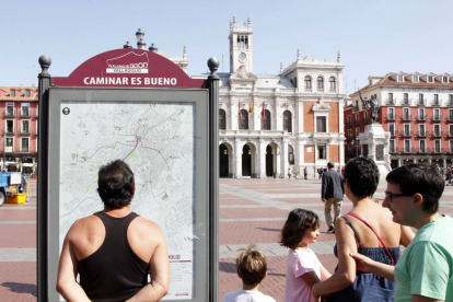 Una familia de turistas observa el panel informativo de las rutas 'Caminar es bueno' en la Plaza Mayor de Valladolid-Ical