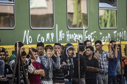 Grupos de refugiados piden continuar su viaje, junto a una valla frente al tren detenido, este viernes en Bcske.-EFE / BALAZS MOHAI