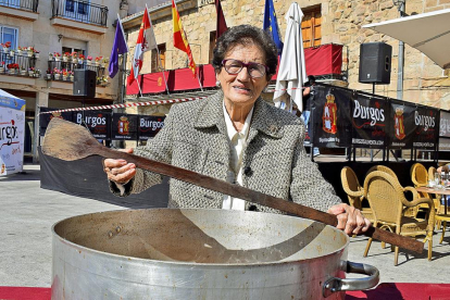 La cocinera arandina Sery Bermejo, junto a un guiso tradicional, en la Plaza Mayor de Salas de los Infantes, donde hace unos días recibió un homenaje junto a otras veteranas cocineras que han hecho historia en la cocina de la provincia de Burgos.-ARGICOMUNICACIÓN