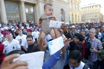 REUTERS / LASZLO BALOGH 

Un inmigrante sirio levanta a su hijo ante la policía húngara para pedir que reabran la estación de trenes de Keleti mientras otros muestran sus billetes.