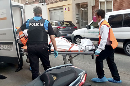 Dos operarios retiran el cuerpo de una de las víctimas en la calle Linares, acompañados por un agente. SGC