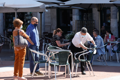 Un trabajador de una cafetería limpia las sillas mientras dos clientes esperan. J.M. LOSTAU