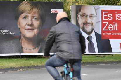 Un ciclista pasa frente a dos carteles electorales de Merkel (izquierda) y Schulz, en Essen, el 14 de septiembre.-AP / MARTIN MEISSNER