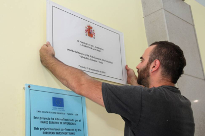 Un operario coloca la placa conmemorativa de la inauguración de la línea de Alta Velocidad en la estación de Palencia, con el nombre de Palencia corregido.-ICAL