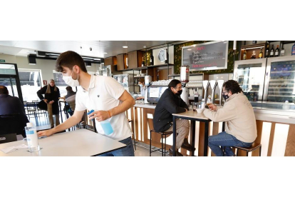 Un camarero desinfecta la mesa en el Café Villa de Prado el día antes del cierre del interior de la hostelería mientras unos clientes disfrutan de su consumición. / J.M. LOSTAU