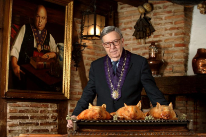 Alberto Cándido López, hijo del mesonero Cándido, con los cochinillos asados que han dado la vuelta al mundo, sobre las andas, y un retrato de su padre detrás, en el Mesón de Cándido de Segovia.-ARGICOMUNICACIÓN