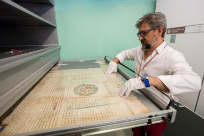 A la izquierda, imagen del documento más antiguo que se conserva. Arriba, el director del Archivo Municipal manipulando un pergamino medieval.-PABLO REQUEJO