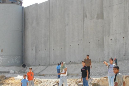 Niños palestinos de camino a la escuela, junto al muro construido por Israel cerca de Qalqilya (Cisjordania).-AP / MOHAMMED AZBA