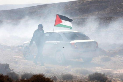 Un hombre ondea la bandera palestina entre gas lacrimógeno, este domingo durante una protesta en el pueblo cisjordano de Shiyoukh, cercano a Hebrón.-ABED AL HASHLAMOUN (EFE)
