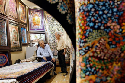 Dos hombres iranís conversan dentro de su negocio de alfombras en el Gran Bazar de Teherán. /-EFE / ABEDIN TAHERKENAREH