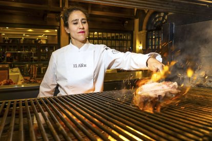Vanesa Martín maneja las llamas de su flamante parrilla en El Alfoz para cocinar una chuleta. Tras ella, el salón en el que los comensales pueden apreciar su trabajo.