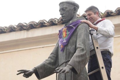 Un operario coloca el pañuelo festivo a la estatua de San Pedro Regalado en Valladolid, símbolo de la celebración de su festividad cada 13 de mayo