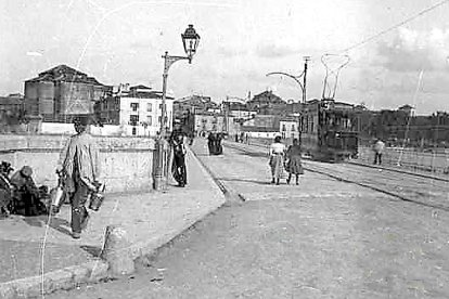 Puente Mayor desde la Plaza de San Bartolomé en 1920. Se aprecia un tranvía, el convento de San Nicolás y otros edificios desaparecidos en la otra orilla. Un lechero, oficio ya desaparecido, va a cruzar el puente, y un uniformado, posiblemente un guardia o un sereno, se aposta junto a la farola, mientras otros personajes están sentados a la derecha. La imagen formaba parte de una tarjeta con otra similar, para posibilitar una visión estereoscópica. ARCHIVO MUNICIPAL