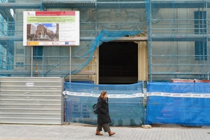 Una viandante pasa por delante del cartel donde se aprecia el precio inicial de la rehabilitación.- J.M. LOSTAU