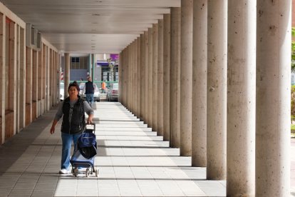 Una mujer con su carro de la compra pasa por debajo de un soportal del Paseo de San Vicente.