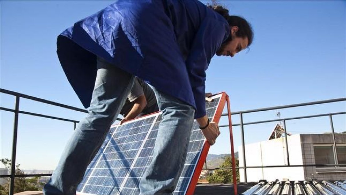 Un hombre instala placas fotovoltaicas en la cubierta de un edificio.-ARCHIVO / JOAN PUIG