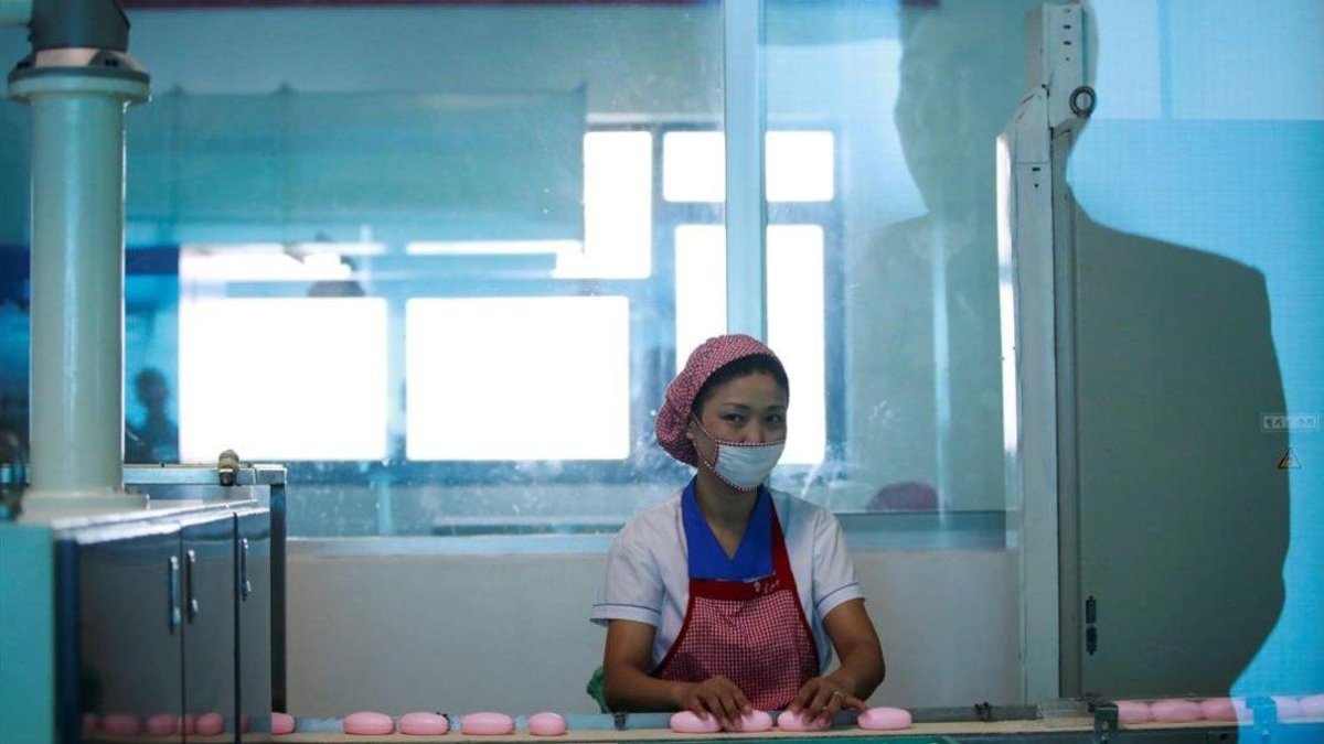 La silueta de un hombre aparece reflejada en el cristal mientras una empleada norcoreana trabaja en la cadena de produccion de jabones de la Fabrica de Cosmética de Pionyang, el 8 de septiembre del 2018.-EFE