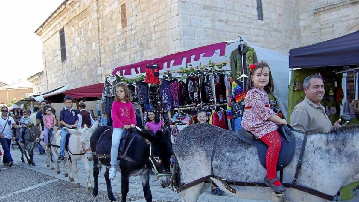 Los niños pasean en burro por delante de los puestos del mercado de oficios.-D. V.