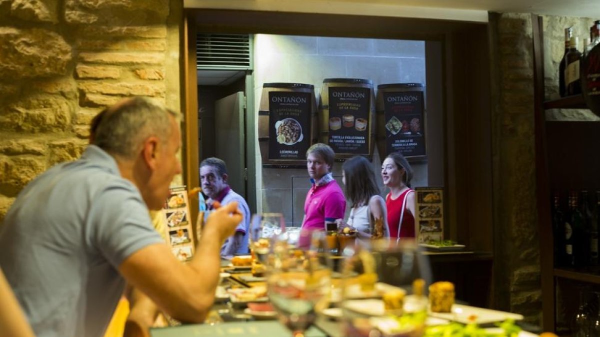Clientes degustan diversas tapas acompañadas de sus vinos en la barra de un bar.