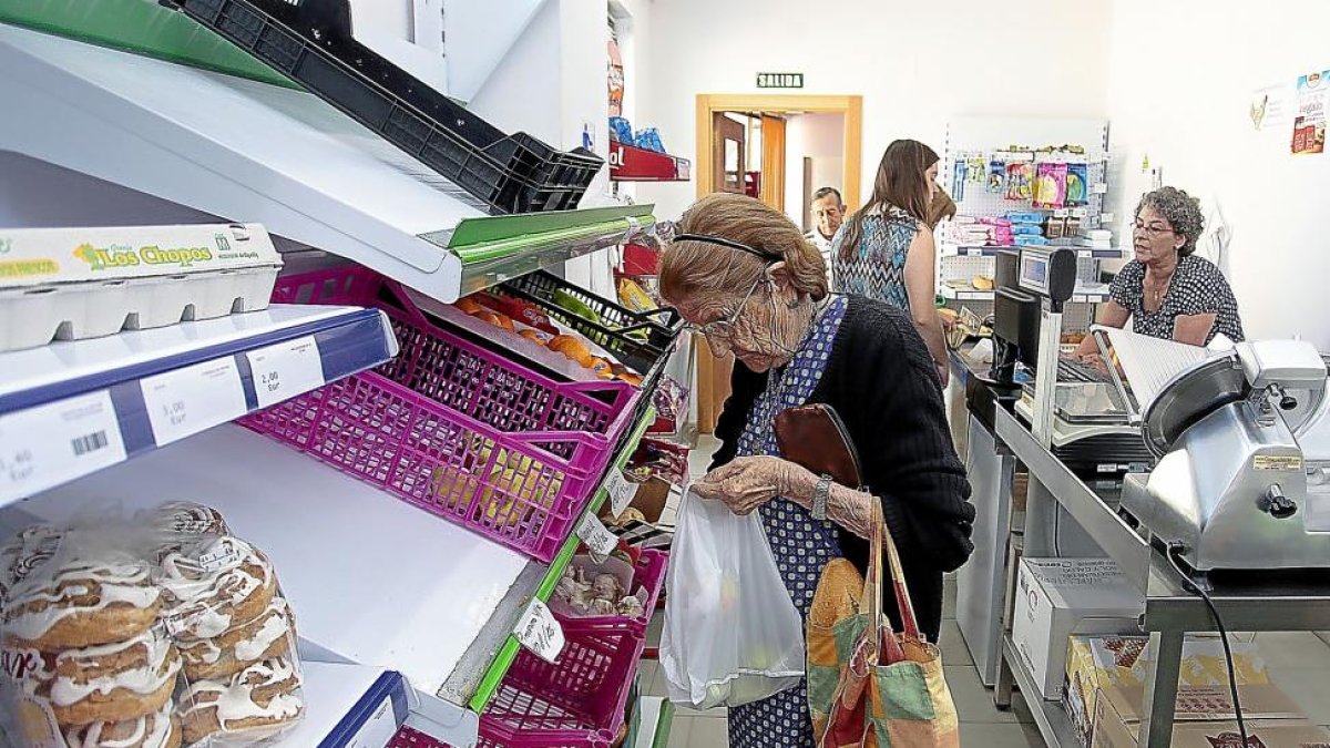 Teresa, una asidua del establecimento de Pedrosa del Rey, escoge fruta para comprar mientras Lali cobra a dos clientas junto a la caja registradora.-JOSÉ CASTILLO