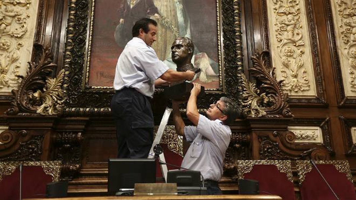 Dos operarios retiran el busto del rey Juan Carlos del salón de plenos del Ayuntamiento de Barcelona.-Foto: DANNY CAMINAL