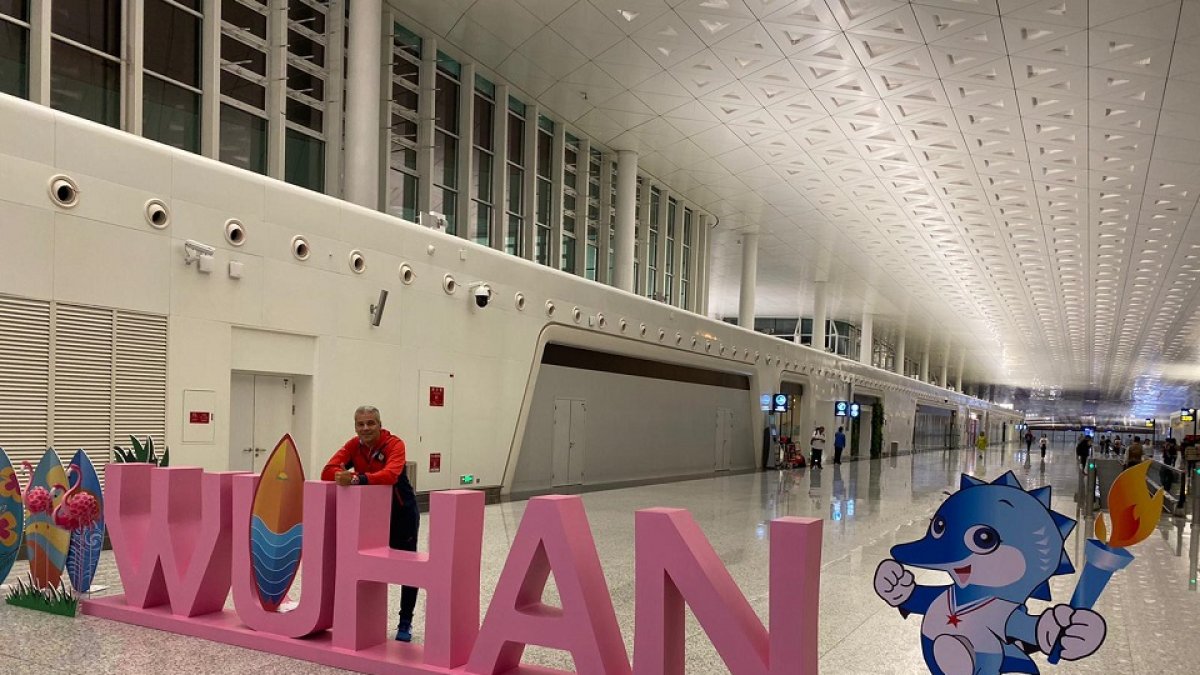Dani Bravo posa en un desértico terminal del aeropuerto junto a un cartel de Wuhan y la mascota de los Juegos.  EL MUNDO