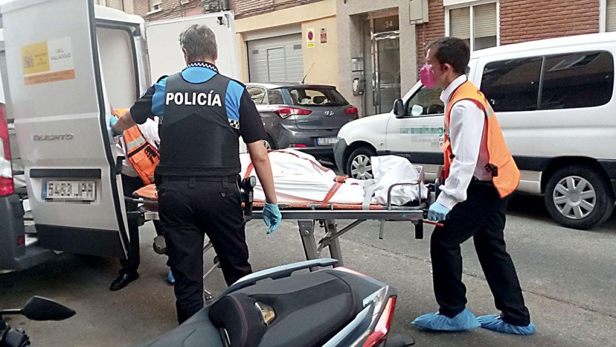 Dos operarios retiran el cuerpo de una de las víctimas en la calle Linares, acompañados por un agente. SGC