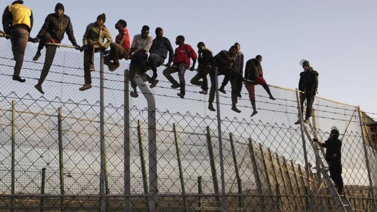 Policías españoles tratan de disuadir a inmigrantes encaramados a la valla de Melilla, fronteriza con Marruecos.-EFE / FRANCISCO G. GUERRERO