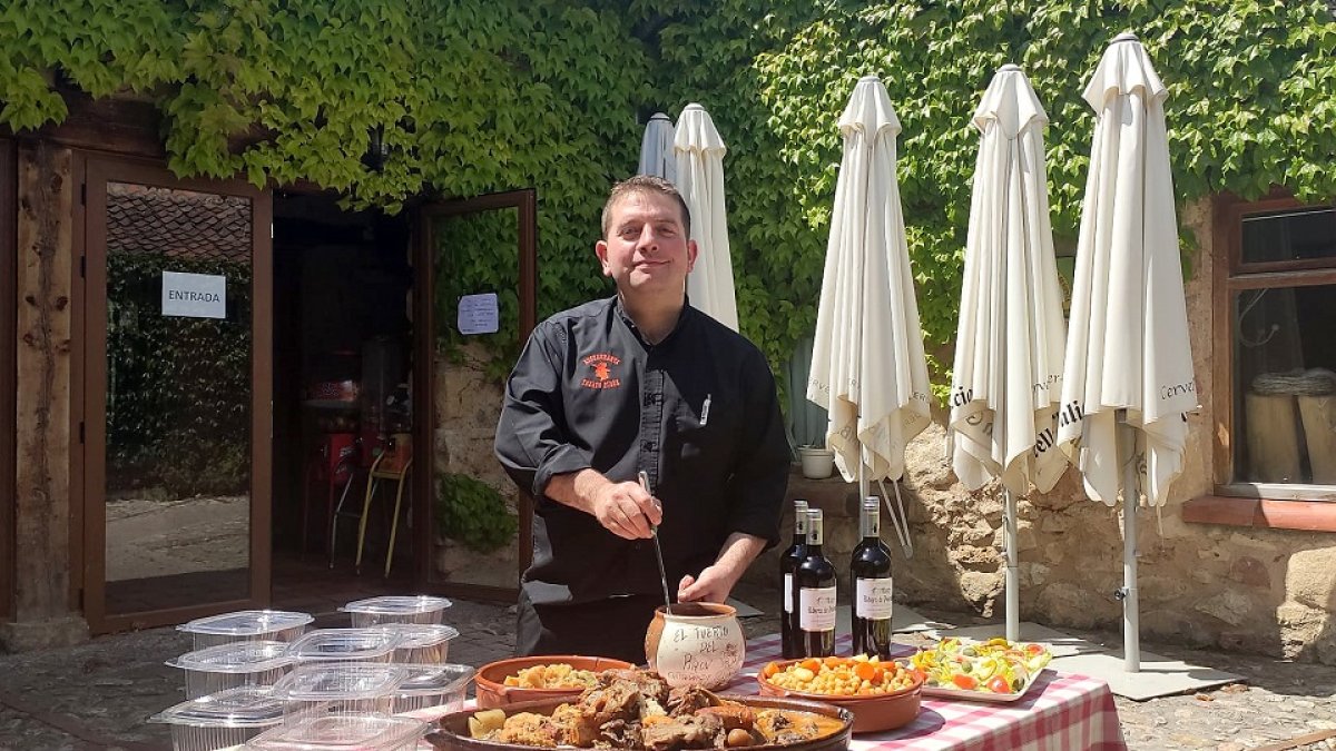 Rubén Martín, en el patio de su restaurante, con uno de sus famosos cocidos y los táperes preparados para llevar.