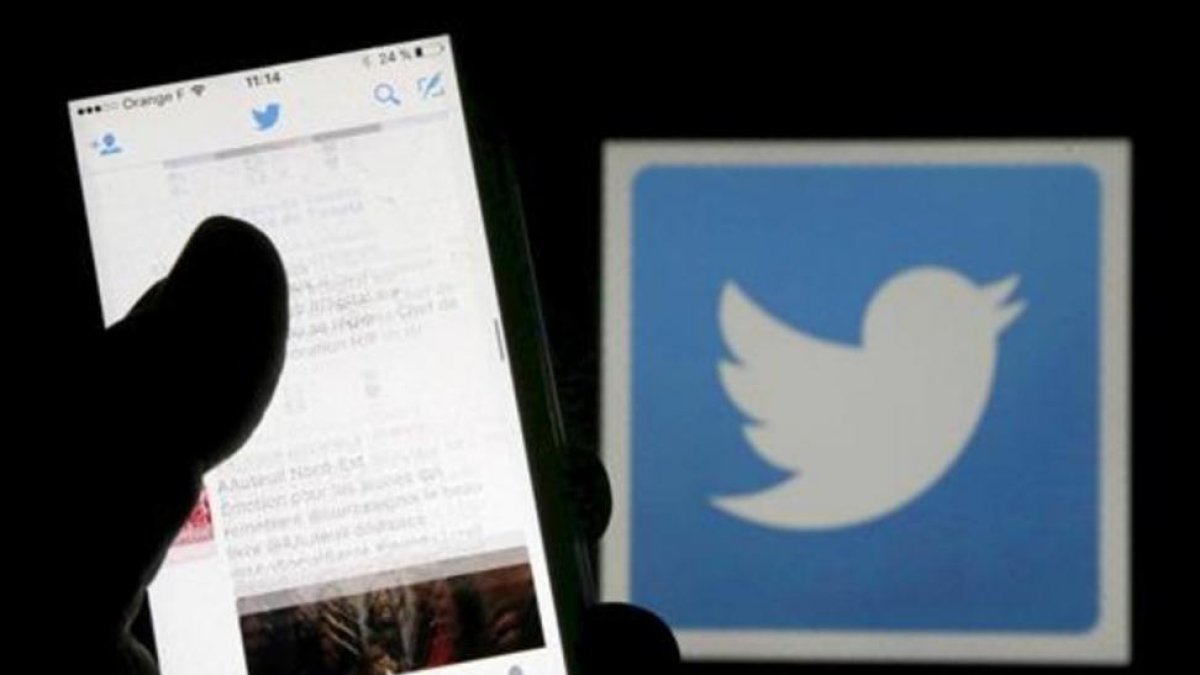 Un usuario de Twitter lee mensajes de esta red social en el móvil frente al logo del pájaro, símbolo de la misma.-/ REUTERS / REGIS DUVIGNAU