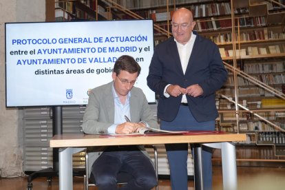 Carnero observa mientras Martínez-Almeida firma el protocolo.