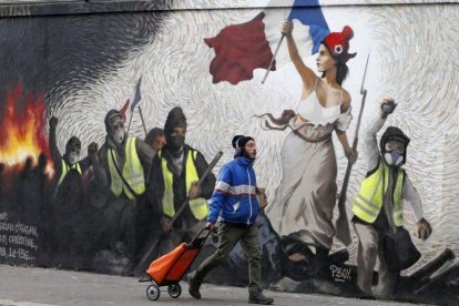 Un hombre pasa junto a un mural que reproduce una versión de La libertad guiando al pueblo, de Eugene Delacroix, con la presencia de chalecos amarillos, idea del artista Pascal Boyart.-GETTY IMAGES