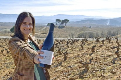 Adriana Ulibarri, con uno de los tintos de la bodega, en el lugar donde se emplazará la futura bodega, en las laderas de Valtuille de Arriba.-ARGICOMUNICACIÓN