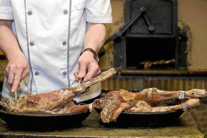 Un asador trincha el lechazo durante la elaboración del alimento en horno de leña.- E. M.