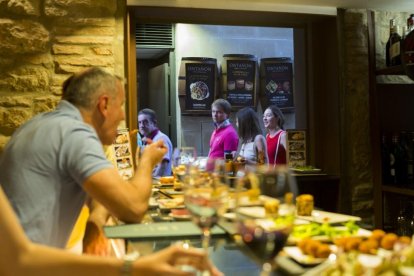 Clientes degustan diversas tapas acompañadas de sus vinos en la barra de un bar.