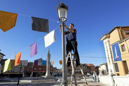 El párroco de Villalón, Francisco Casas, coloca los banderines en la plaza junto a El Rollo, tras haber instalado un gran cartel de ‘Holywins’.-J. M. LOSTAU