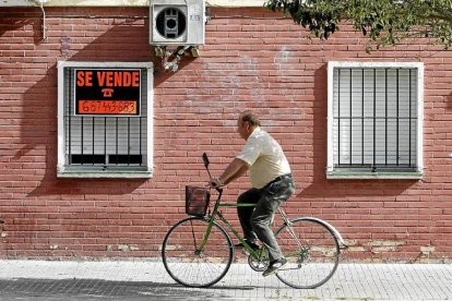 Un hombre en bicicleta pasa por delante de un cartel de 'Se vende' en una vivienda.-Carlos Márquez