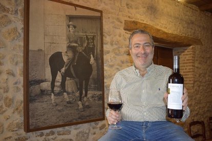 Ricardo Rodilla enseña una botella en el interior de la bodega tradicional ante la mirada de una foto de su madre, Társila a caballo.-ARGICOMUNICACIÓN