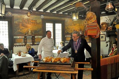 Alberto López (d) y su hijoCándido trinchan un cochinillo en una sala del mesón.-I. M.