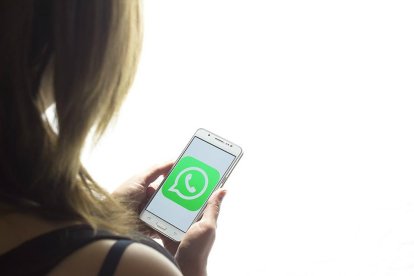 Una chica mira la pantalla de su teléfono móvil, con el logo de Whatsapp.-EL PERIÓDICO